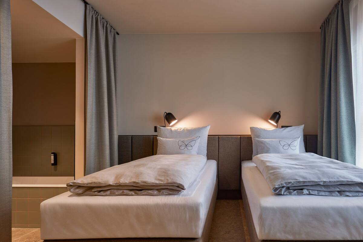 A hotel room with two beds, each with a pillow featuring a butterfly design, a bedside lamp, and a neutral color scheme.