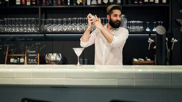 A bartender preparing a drink behind a bar with shelves of bottles and glasses.