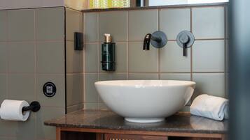 Une salle de bain avec un grand lavabo blanc, une serviette, un porte-rouleau de papier toilette et un distributeur de savon pour les mains.