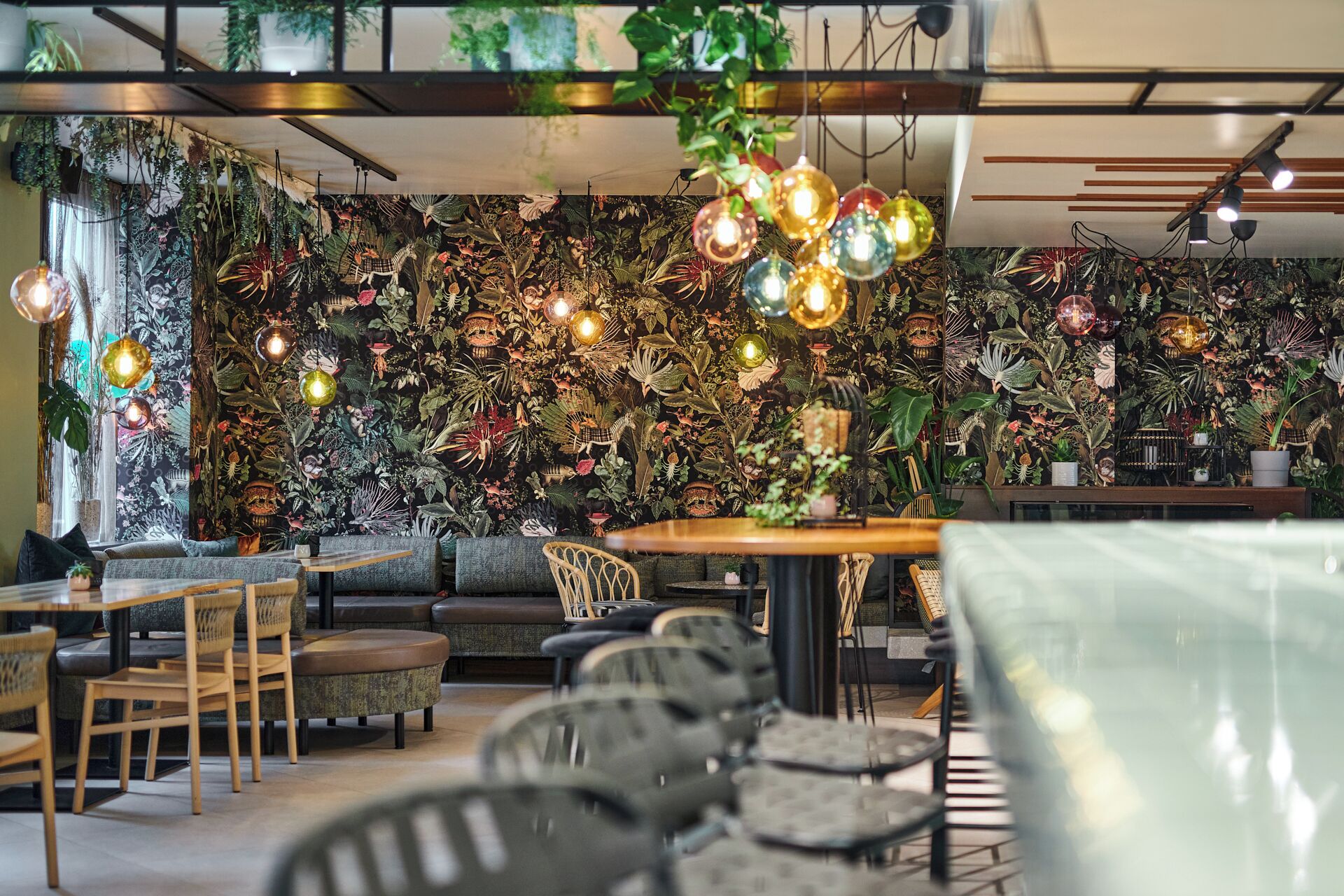 L’intérieur d’un restaurant, avec un mur recouvert de plantes suspendues, des meubles en bois et des luminaires suspendus.