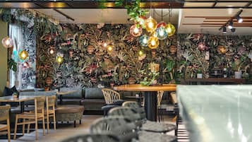 L’intérieur d’un restaurant, avec un mur recouvert de plantes suspendues, des meubles en bois et des luminaires suspendus.
