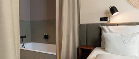 Een hotelkamer met een badkuip, nachtkastje, lamp en een bed met een kussen met vlinderprint.