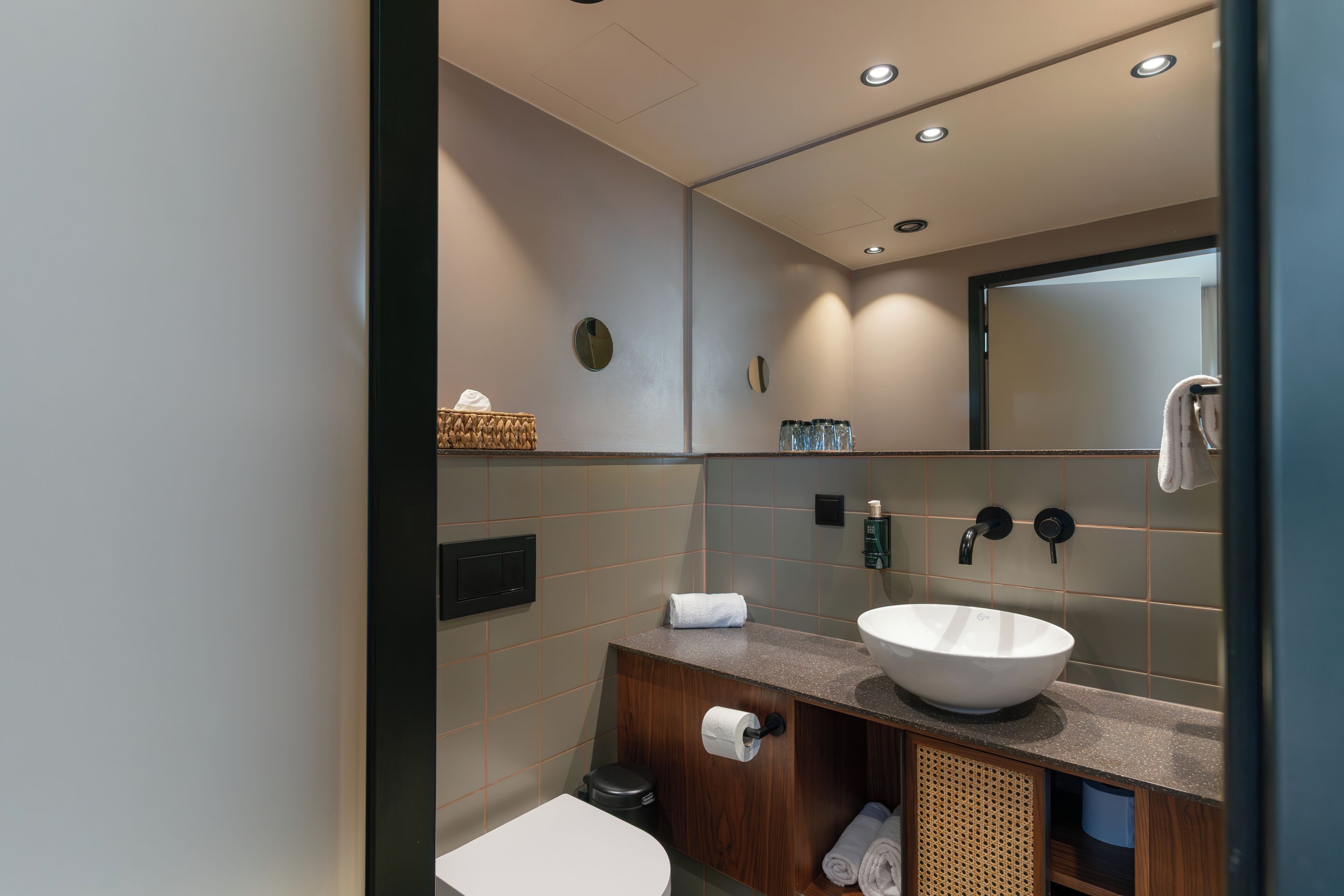 Un baño moderno con un lavamanos blanco, tocador de madera y un espejo.