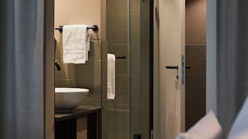 Baño de hotel con ducha acristalada, lavamanos y perchero.