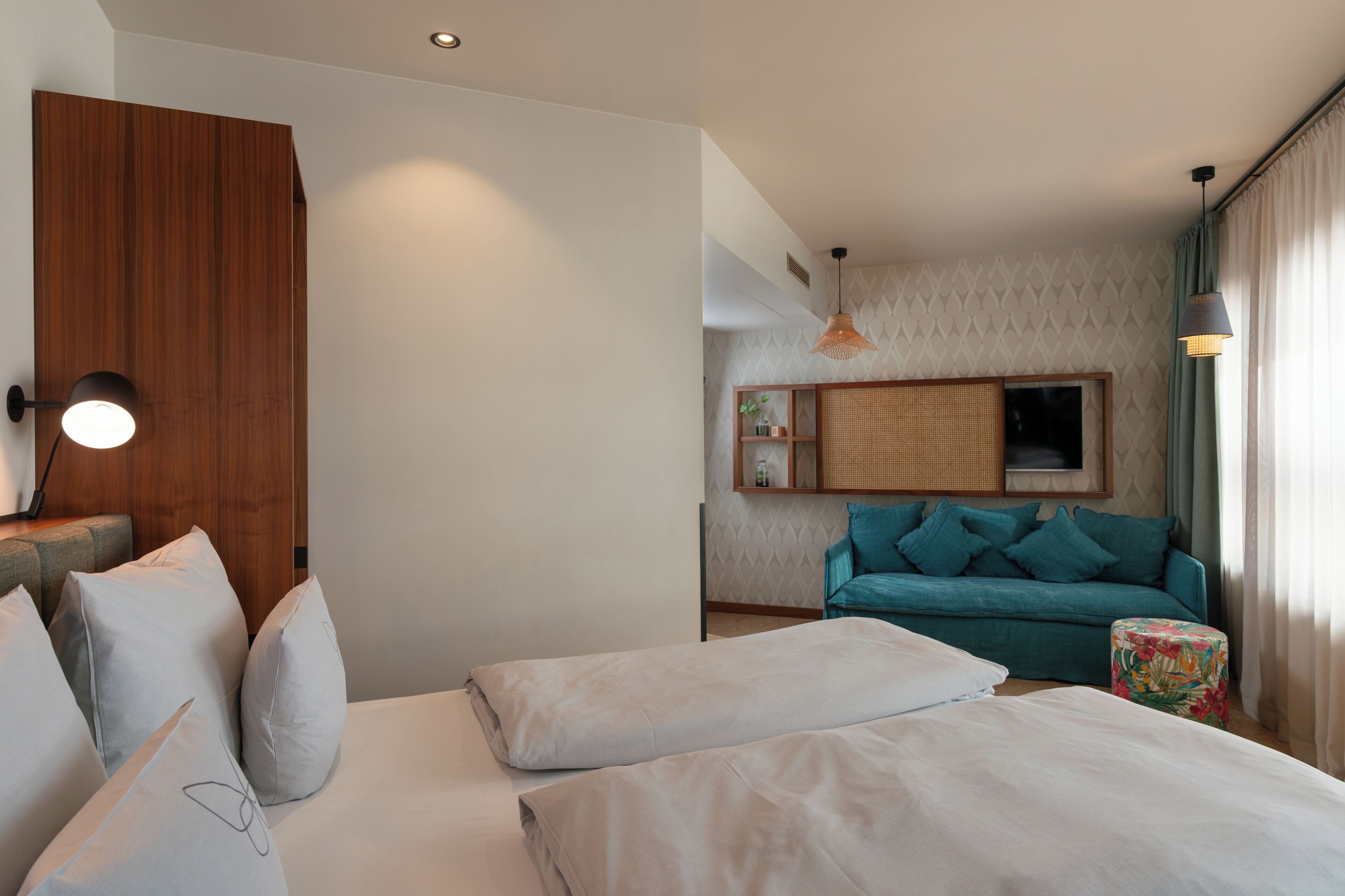 Een moderne hotelkamer met een bed, een houten garderobe, een blauwgroene bank en een klein tafeltje met een bloemrijk tafelkleed.