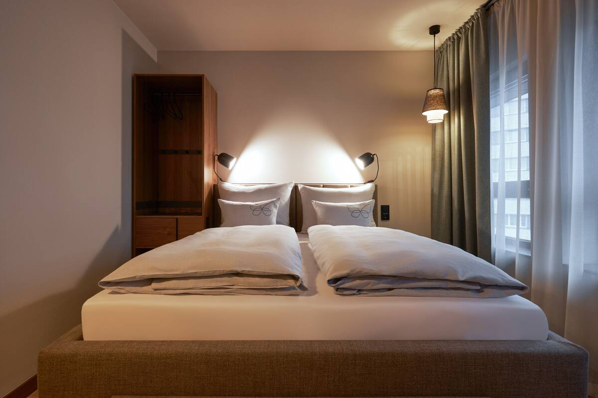 A neatly made bed with pillows, a bedside lamp, and a wooden wardrobe in a hotel room.