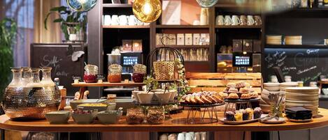 A café with a variety of food and drink options, including jars of preserves, a display of pastries, and a seating area with stools.