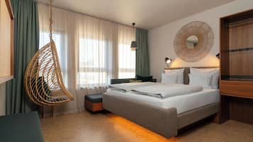 A hotel room with a bed, a hanging chair, a bedside table, a lamp, and a wardrobe.