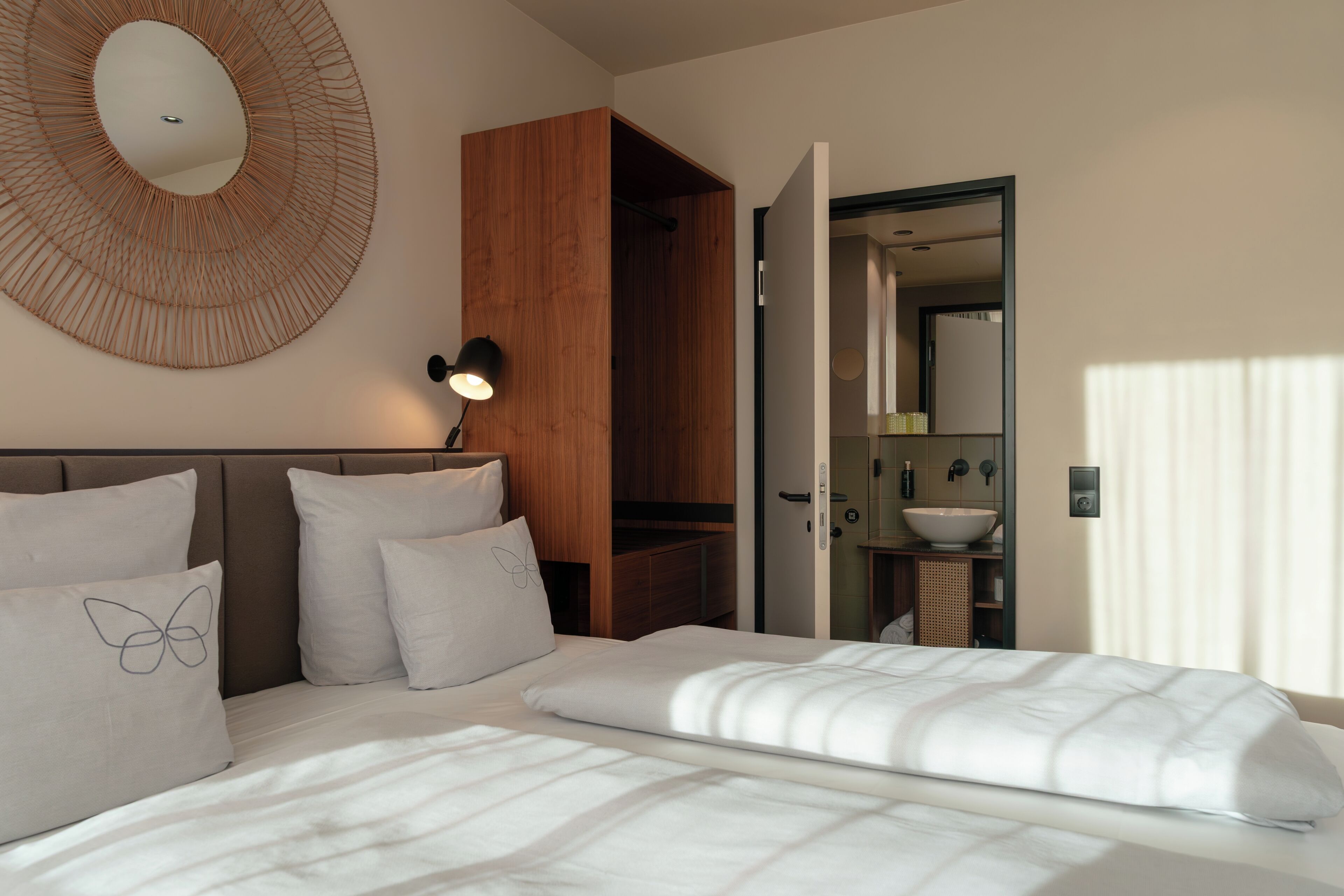Une chambre à coucher moderne avec un lit, des oreillers, une lampe fixée au mur et une armoire en bois.