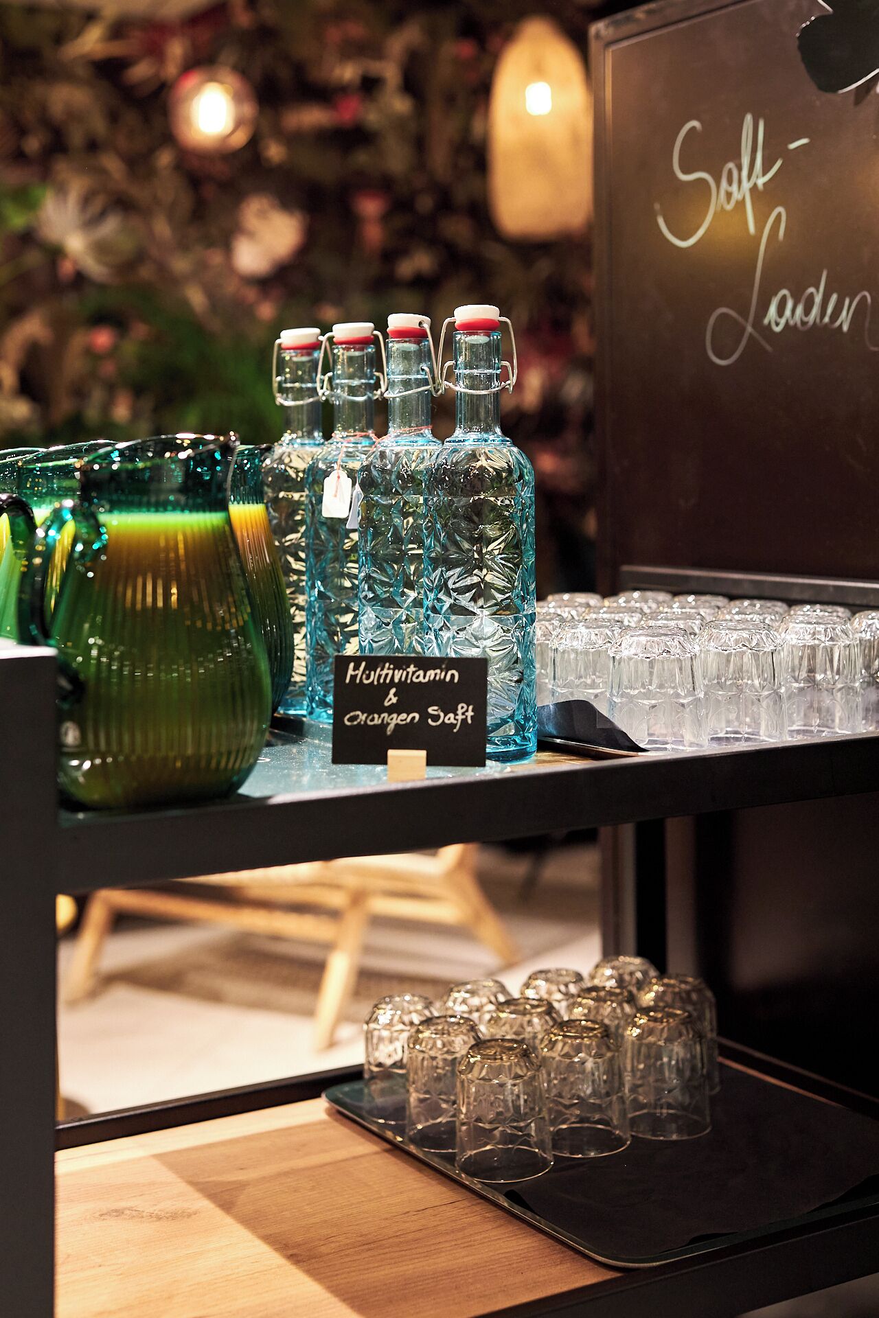 A display of clear glass bottles and glasses on a shelf, with a sign indicating 'Multivitamin & Orange Saft'.