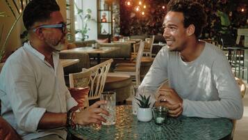 Two individuals seated at a round table with a glass and a small potted plant.