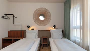 Habitación de hotel con dos camas, un espejo redondo montado en la pared, perchero, lámparas de noche y ventana con cortinas.