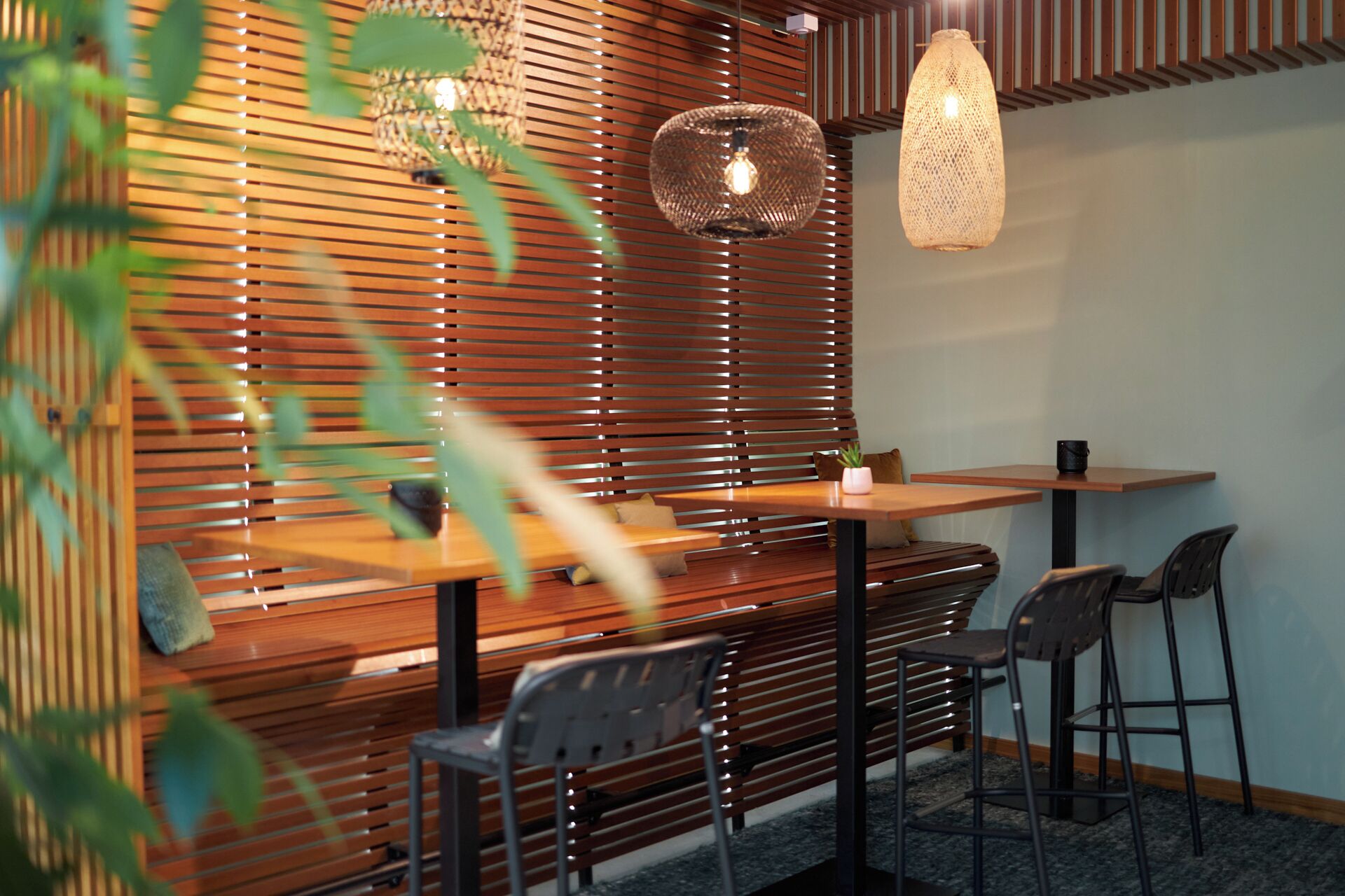 Un interior moderno con un muro de listones de madera, una lámpara colgante redonda y una mesa con sillas.