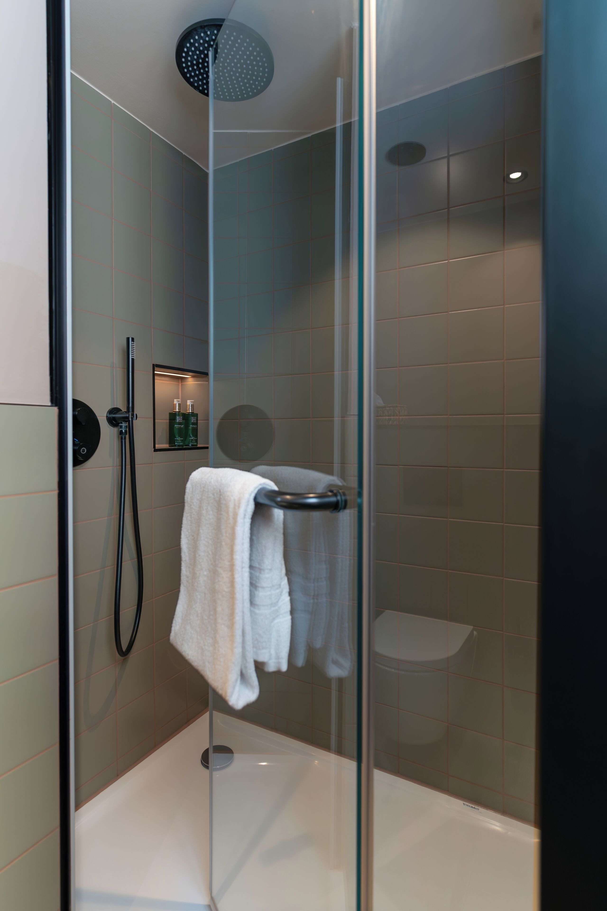 Een moderne douchecabine met een glazen deur, een handdouche en een handdoekhouder.