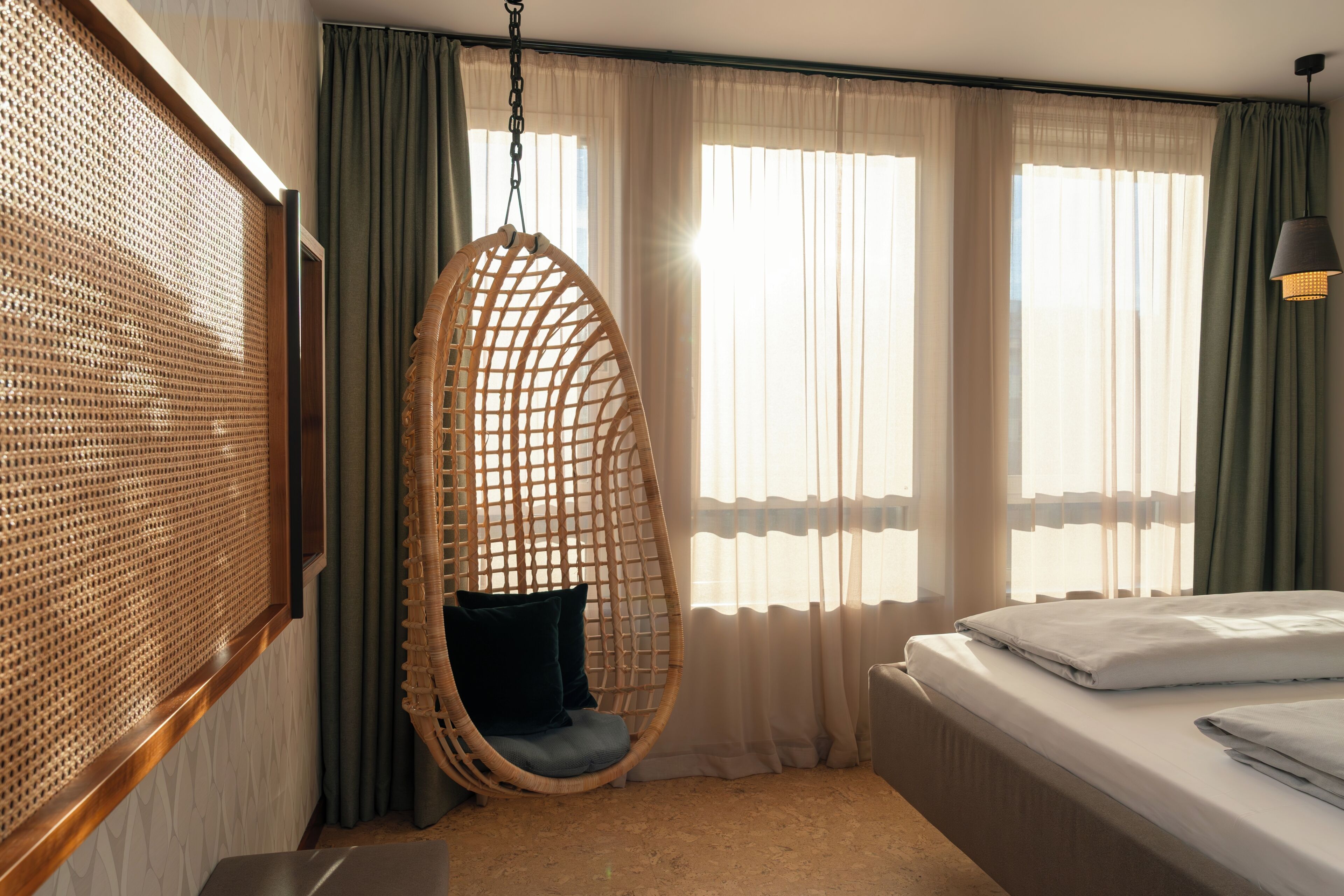 A room with a hanging chair, a bed, and a window with curtains.