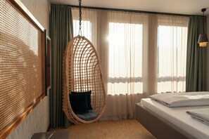 A room with a hanging chair, a bed, and a window with curtains.