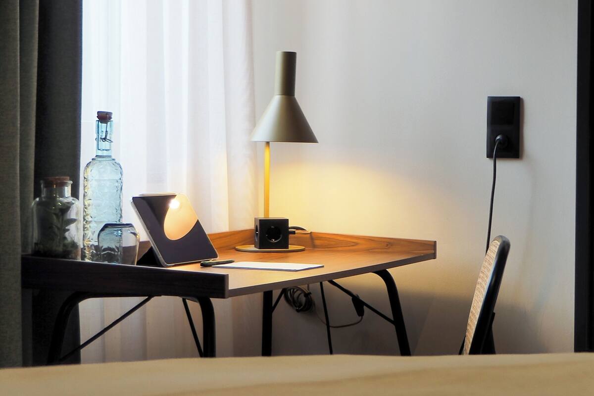 A wooden desk with a lamp, a tablet, and a speaker. There is a bottle and a cup on the desk.