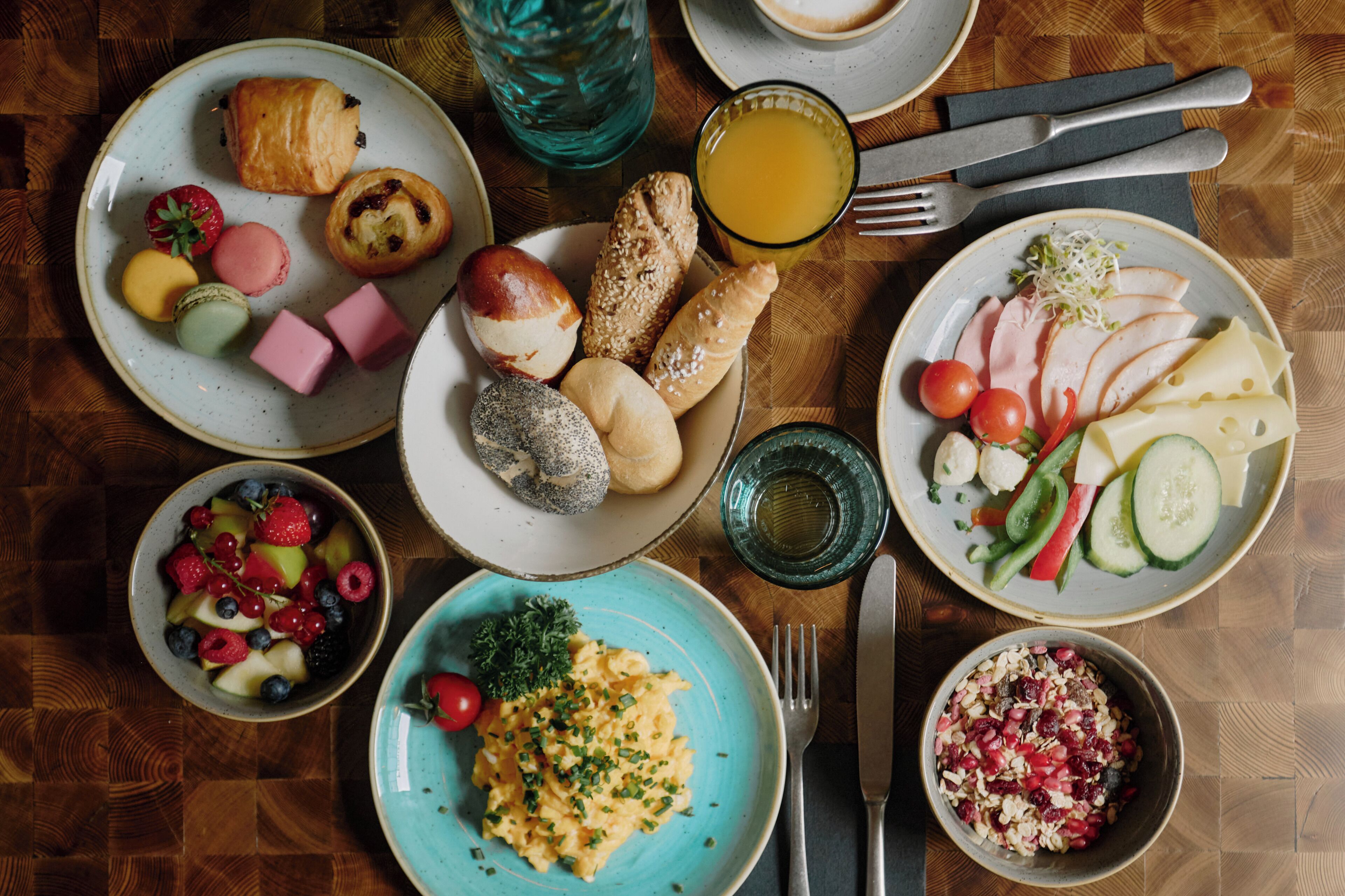 Une table dressée pour le petit-déjeuner, avec différents plats, notamment des œufs, des viennoiseries et des fruits.