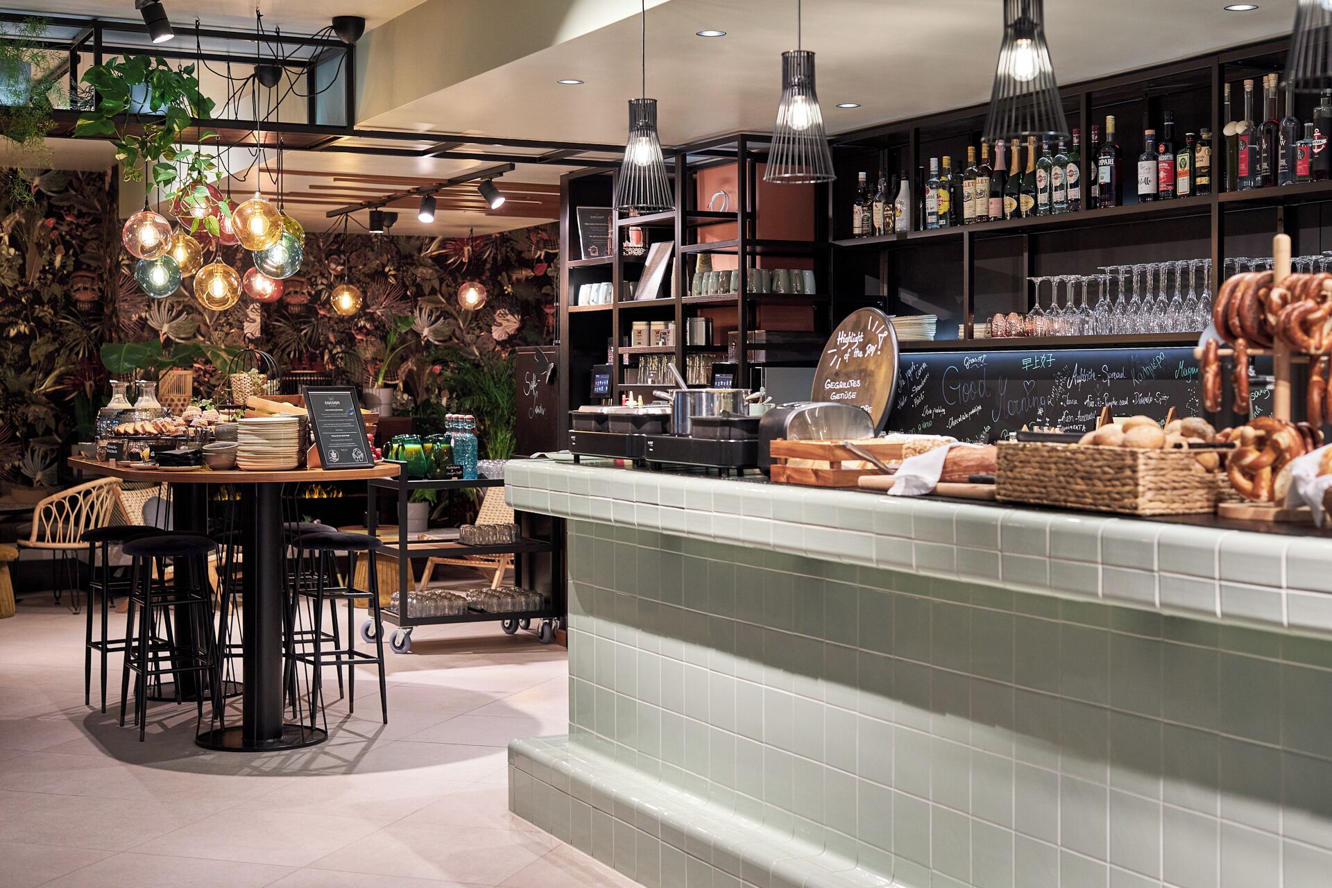 A bar area with a counter displaying snacks and drinks, shelves with bottles, and hanging light fixtures.