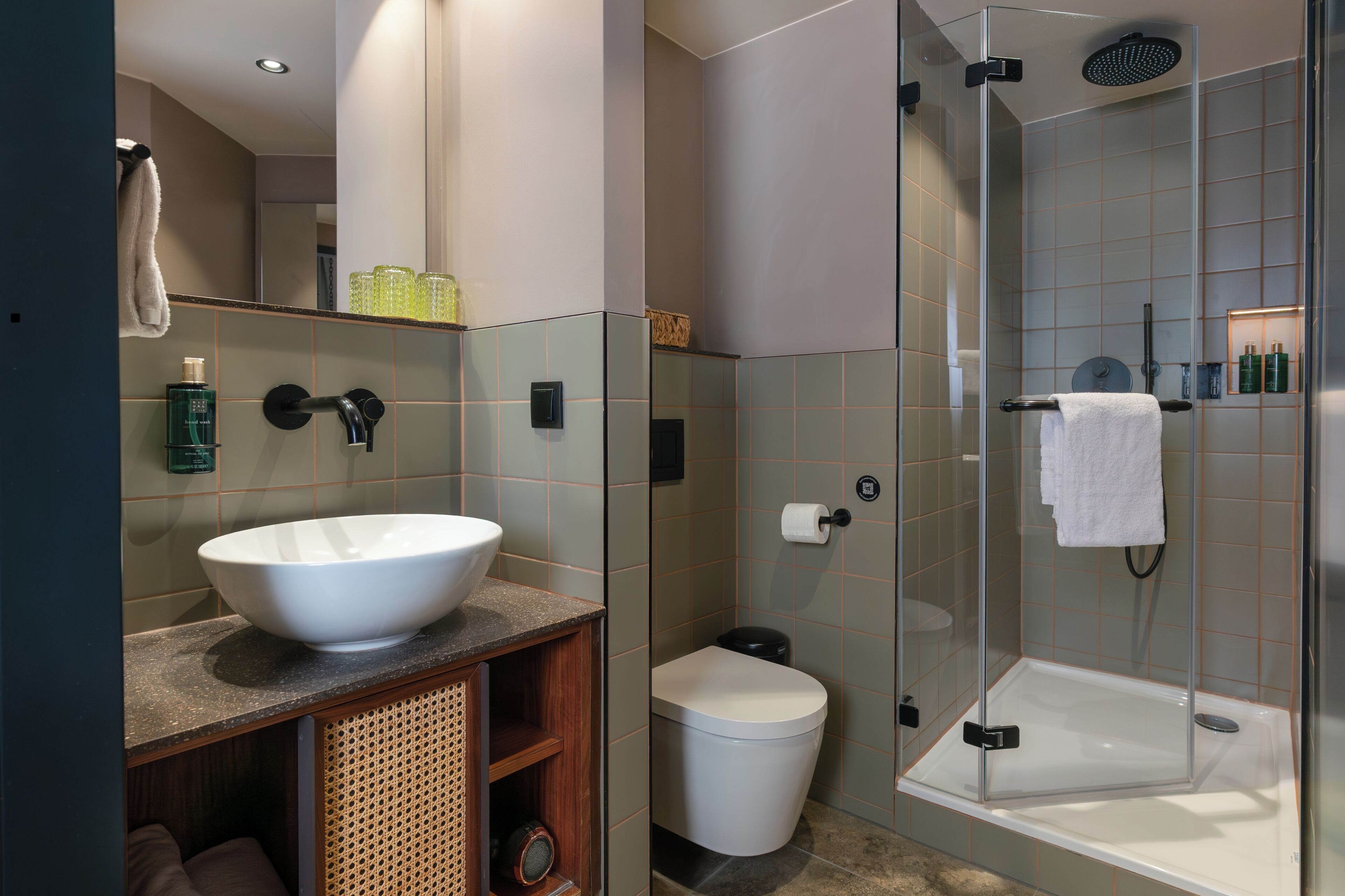 Un baño moderno con un lavamanos grande de color blanco, una ducha con mampara de vidrio y un inodoro.