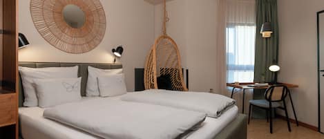 A hotel room with a bed, a desk, a chair, a hanging chair, and a large mirror.