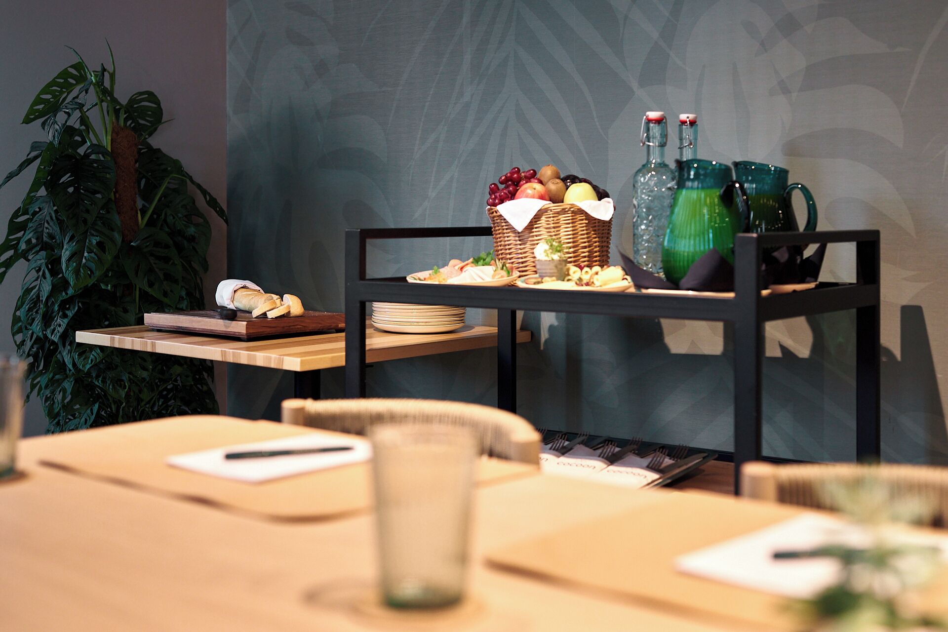 A dining area with a table set for a meal, a plant, and a buffet cart with food and drinks.