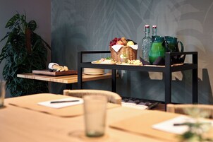 Un comedor con una mesa lista para comer, una planta y un carrito de buffet con comida y bebidas.