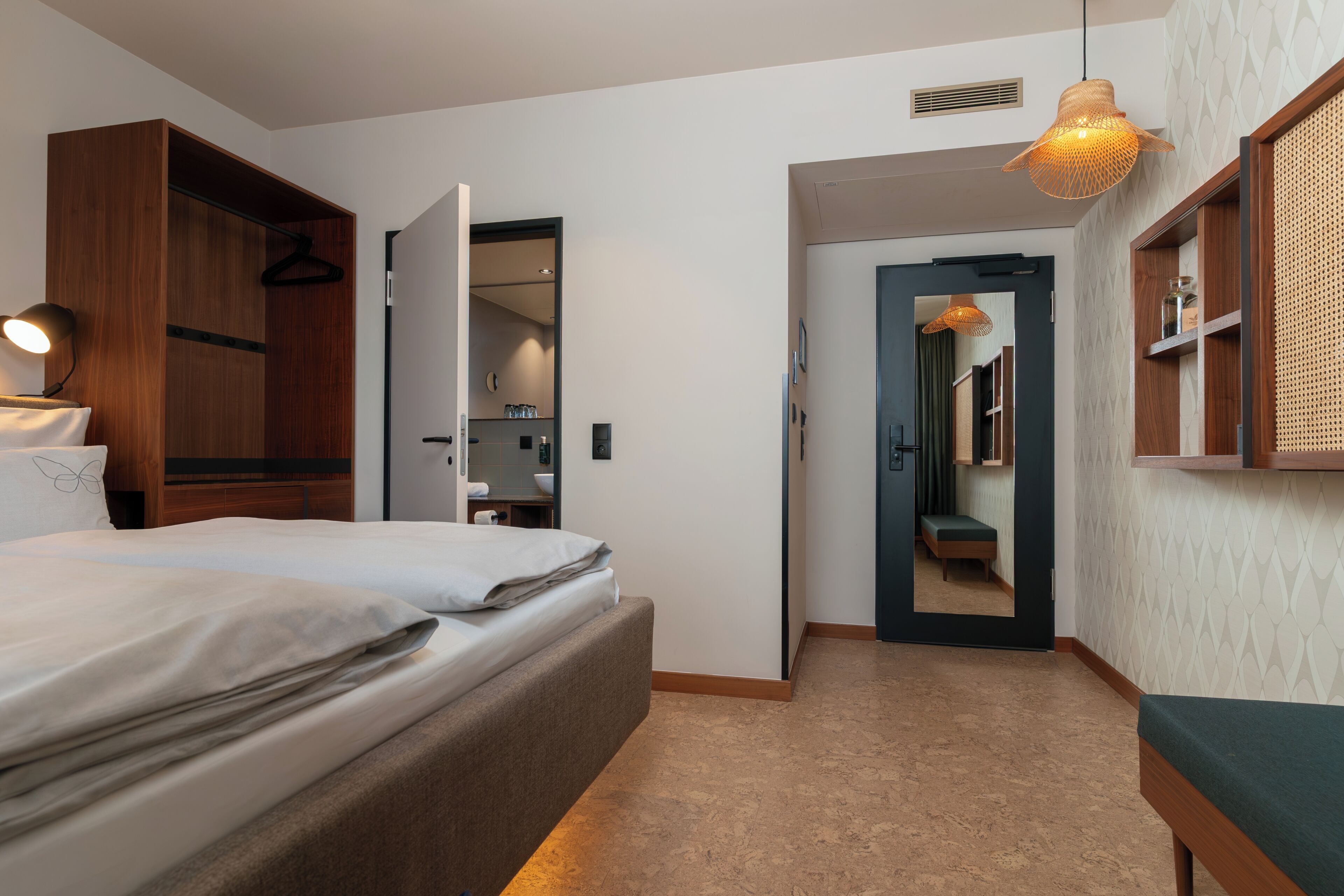 Une chambre d’hôtel avec un lit, un luminaire suspendu et une porte donnant accès à une salle de bain.