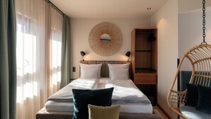 A hotel room with a bed, a large mirror, a hanging chair, and a wardrobe. - Cocoon Salzburg Hauptbahnhof  (Salzburg)