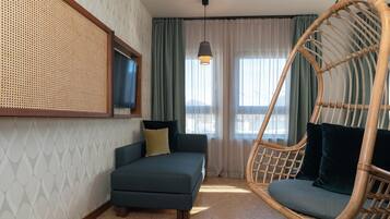 A room with a sofa, a hanging chair, a television, and a window with curtains.