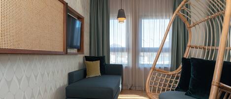 Una habitación con sofá, sillón colgante, televisor y ventana con cortinas.