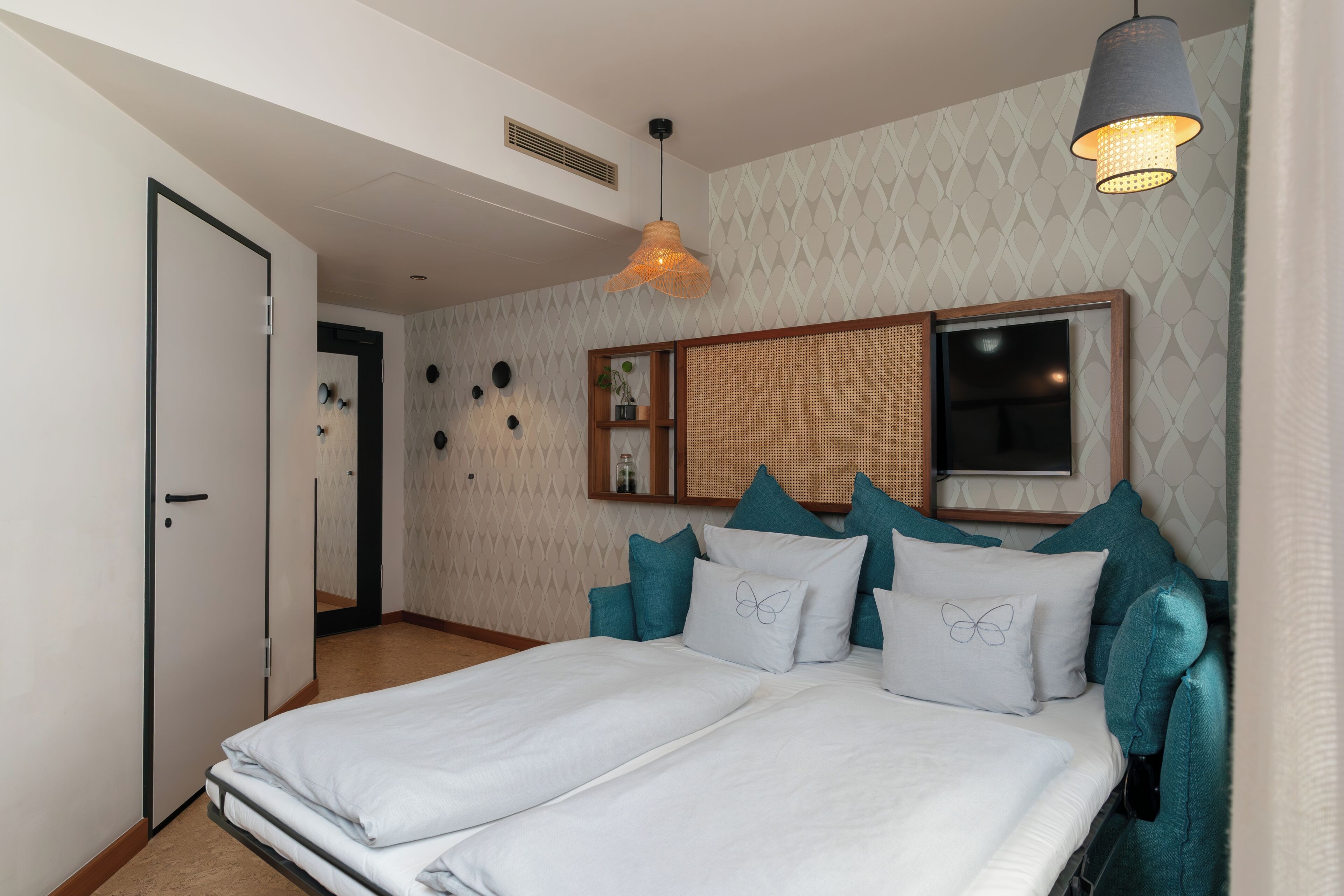 Ein Schlafzimmer mit einem Bett, einer Hängelampe, einem an der Wand montierten Fernseher und Wanddekoration.