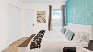 Un dormitorio con cama, banca, puerta y ventana con cortinas.