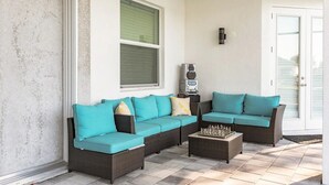 Un espacio de patio techado con un sofá modular, una mesa de centro, un altavoz y una puerta que da al exterior.