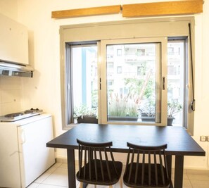 A kitchen with a stove, a window with a view of buildings and plants, and a table with two chairs. - Urban Orange by Domisi with private Jacuzzi (Ρέθυμνο)