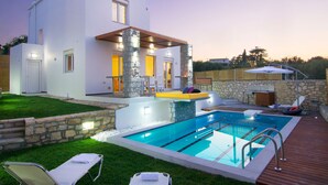 Ett modernt hus med en swimmingpool, utomhusmöbler och en stenmur.