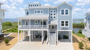 Een twee verdiepingen tellend strandhuis met een balkon, een overdekte veranda en een trap naar de bovenverdieping.