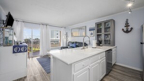 A modern kitchen with a large island, white cabinetry, and a view to the outside. - New Heated Pool & Hot tub! Views plus 2 recliners! (Galveston)