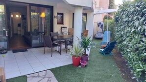 Un patio con tavolo e sedie, un piccolo giardino con erba sintetica e un siepe.