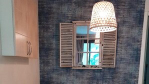 Zona pranzo con tavolo apparecchiato per quattro, circondata da sedie in vimini, un lampadario e una finestra con persiane.