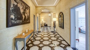 A hotel hallway with a patterned floor, a large world map on the wall, and a bench with candles. - Ta’ Benna Villa Gozo Luxury Accommodation (Ghajnsielem)