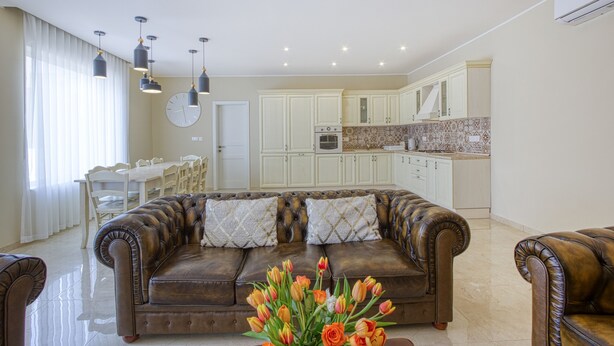A spacious living room with a leather sofa, a dining area with a table and chairs, and a kitchen with white cabinets and a tiled backsplash. - Ta’ Benna Villa Gozo Luxury Accommodation (Ghajnsielem)