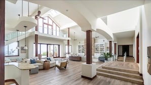 Un'ampia zona giorno con soffitto alto, pavimento in legno e un soppalco con librerie.