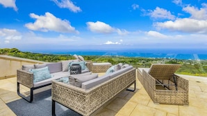 Una terrazza sul tetto con mobili in vimini, vista sull'oceano e cielo sereno.