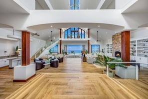 A spacious living area with a high ceiling, a staircase, and a view of the ocean. - Luxury Kona Mansion: Infinity Pool & Epic Views (Kailua-Kona)