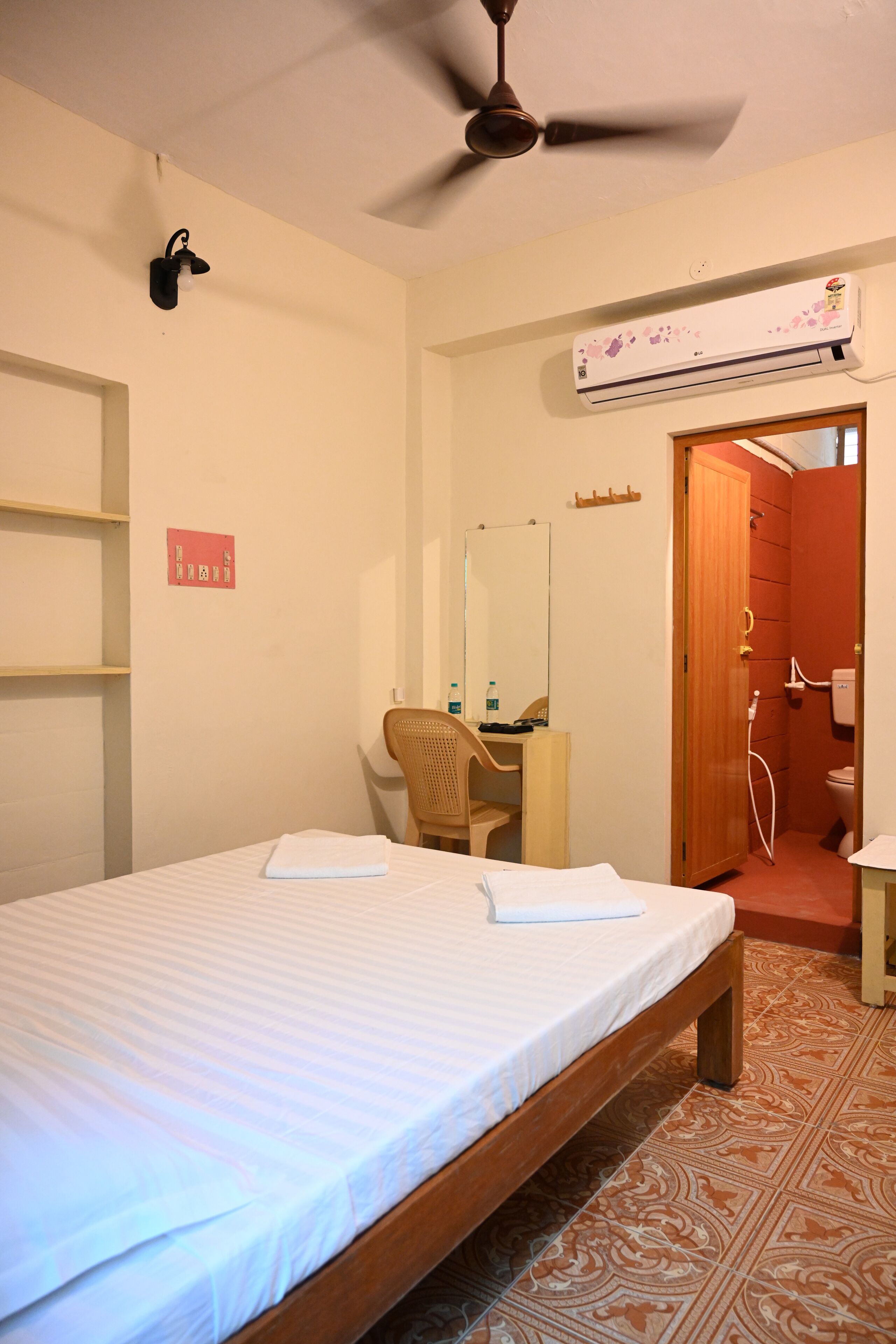 Un dormitorio con cama, escritorio, silla, ventilador de techo, unidad de aire acondicionado y baño con ducha e inodoro.