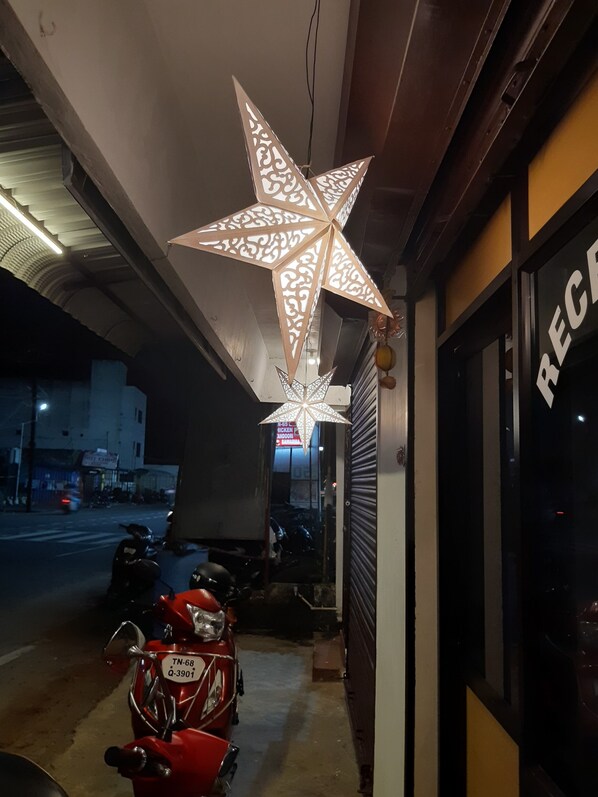 A building with a closed shutter on the right, a star-shaped light fixture hanging from the ceiling, and a red motorcycle parked in front.