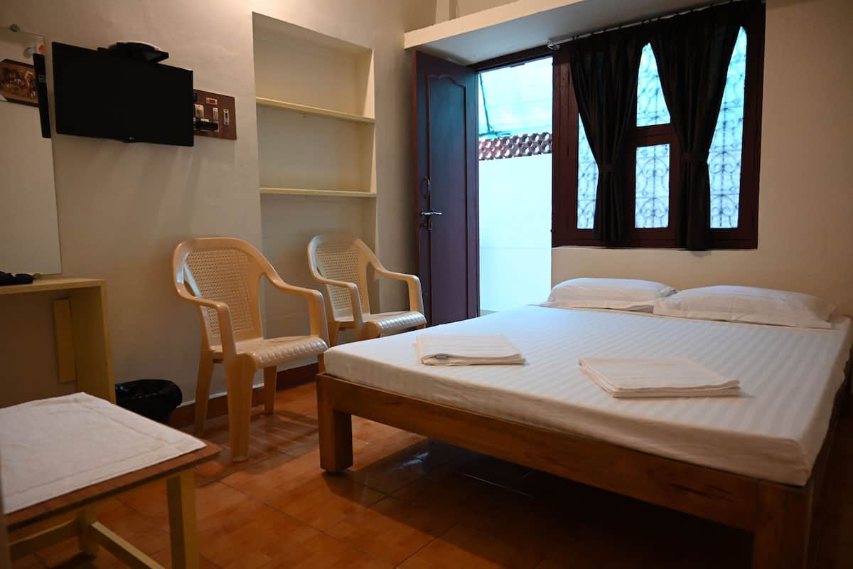 Une chambre à coucher avec un lit, deux chaises, un téléviseur et une fenêtre avec des rideaux.