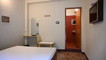 Quarto de hotel com uma cama, uma mesinha, um espelho, uma pia e uma porta que dá para outro quarto.