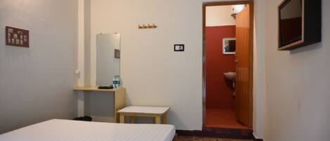 A hotel room with a bed, a small table, a mirror, a sink, and a door leading to another room.